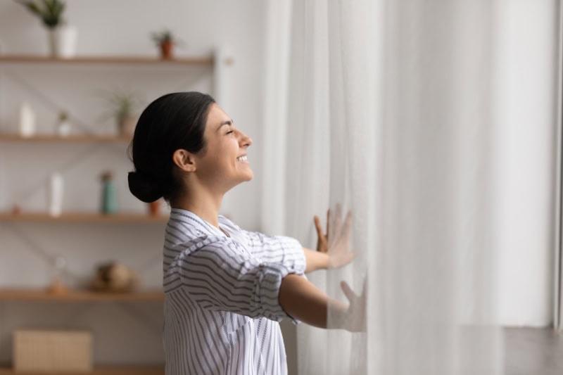 Happy female open drapes on window breath fresh air close eyes in delight.